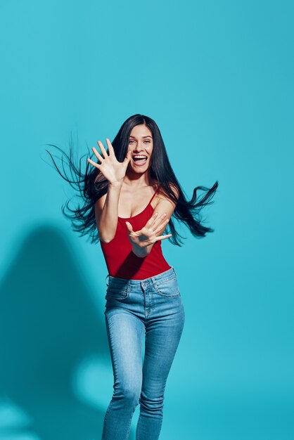 Aantrekkelijke jonge vrouw en glimlachend terwijl ze tegen de blauwe muur staat