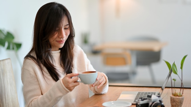 Aantrekkelijke jonge vrouw geniet van haar ochtendkoffie in een co-werkruimte van een café. ontspan voordat je gaat werken