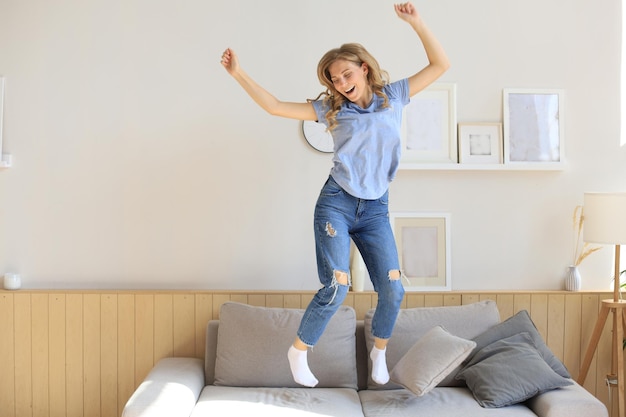 Aantrekkelijke jonge vrouw heeft plezier thuis. Meisje springt en danst op de bank.