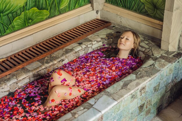 Aantrekkelijke jonge vrouw in bad met bloemblaadjes van tropische bloemen en aroma-oliën Spa-behandelingen voor huidverjonging Verleidelijke vrouw in Spa salon Luxe spa en huidverzorging