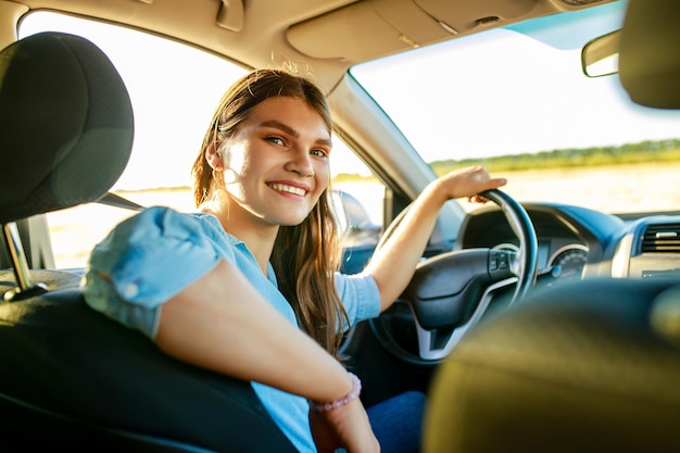 Aantrekkelijke jonge vrouw in blauw shirt bij zonsondergang licht met haar auto