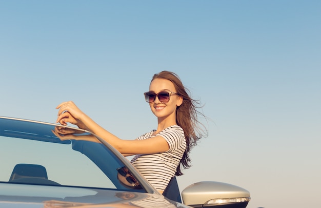 aantrekkelijke jonge vrouw in de buurt van een converteerbare auto