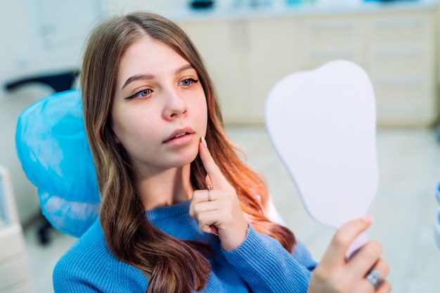 Aantrekkelijke jonge vrouw in de stomatologie kijkt naar de spiegel. Gezond tandenconcept.