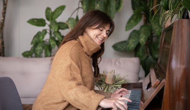 Aantrekkelijke jonge vrouw in een gezellige bruine trui speelt piano.