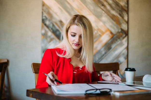 Aantrekkelijke jonge vrouw in een rood jasje werkt aan een tafel met papieren en apparaten