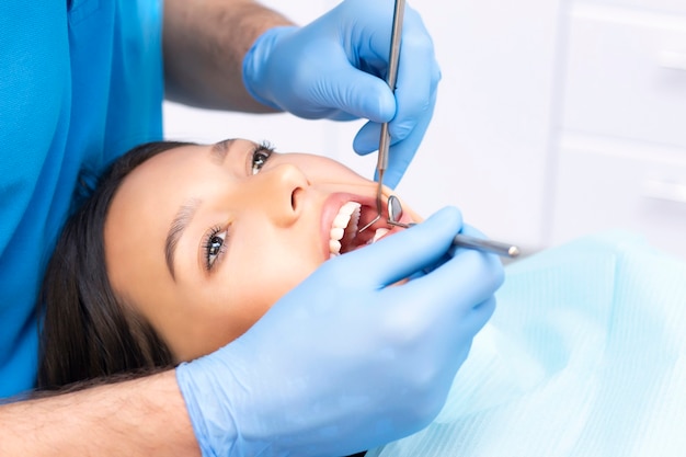 Aantrekkelijke jonge vrouw in een tandheelkundige kliniek met een mannelijke tandarts. Gezond tandenconcept.