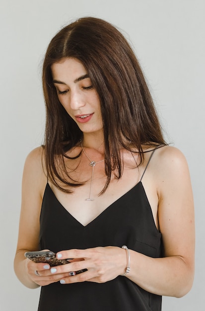 Aantrekkelijke jonge vrouw in een zwart jurkje gebruikt een smartphone voor communicatie en glimlachen