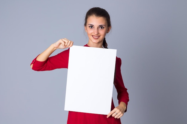 Aantrekkelijke jonge vrouw in rode blouse met wit vel papier op grijze achtergrond in studio