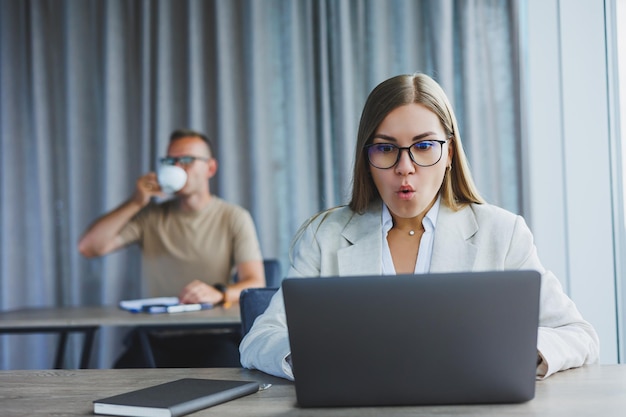 Aantrekkelijke jonge vrouw met een bril zit aan een tafel met een laptop in een coworking-ruimte en bespreekt een projectplan met een collega Workflow op kantoor