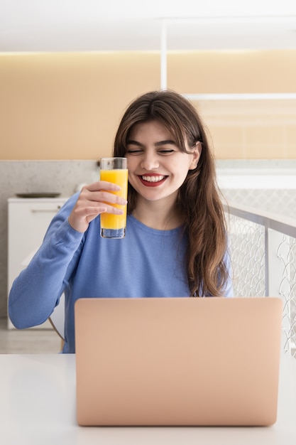 Aantrekkelijke jonge vrouw met een glas sap zit voor een laptop