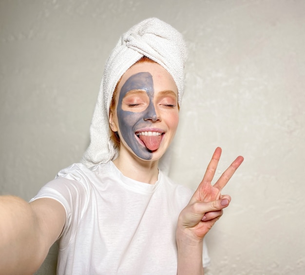 Foto aantrekkelijke jonge vrouw met een handdoek op haar hoofd en een kleimasker