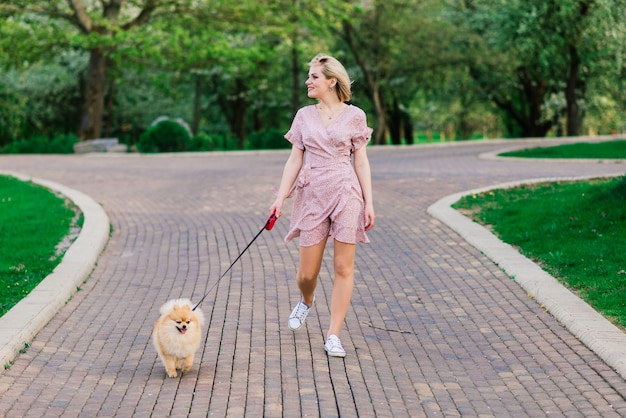 Aantrekkelijke jonge vrouw met hond spitz buiten en glimlachen, wandelen in het park. Begrip over vriendschap tussen mens en dier.