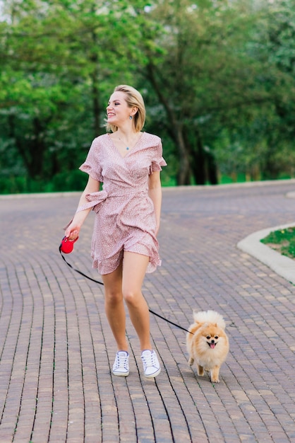 Aantrekkelijke jonge vrouw met hond spitz buiten en glimlachend in de camera, wandelen in het park