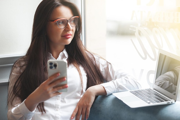 Aantrekkelijke jonge vrouw met laptop Vrouw in cafetaria met gadgets Busuness vrouw binnenshuis