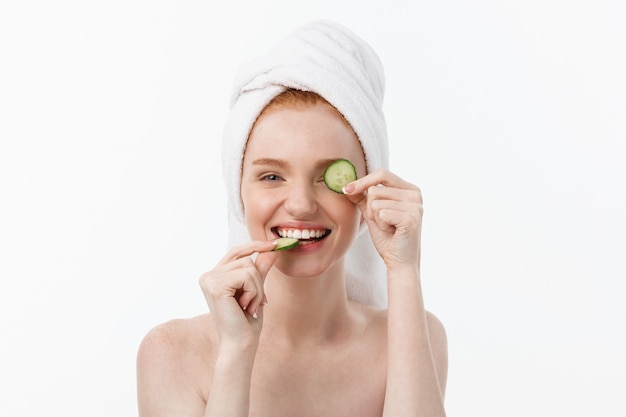 Aantrekkelijke jonge vrouw met mooie schone huid. Wit masker en komkommers. Schoonheidsbehandelingen en cosmetologie spa-therapie.
