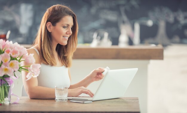 Aantrekkelijke jonge vrouw online winkelen met behulp van computer en creditcard in huis keuken.