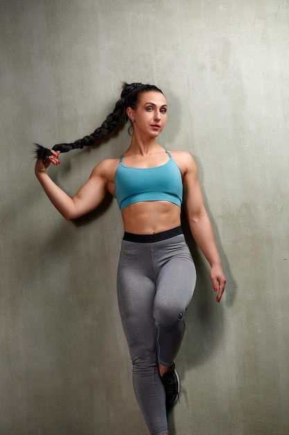 Aantrekkelijke jonge vrouw staat sterk in de sportschool en buigt spieren Mooie atletische fitnessmodel poseren na oefeningen