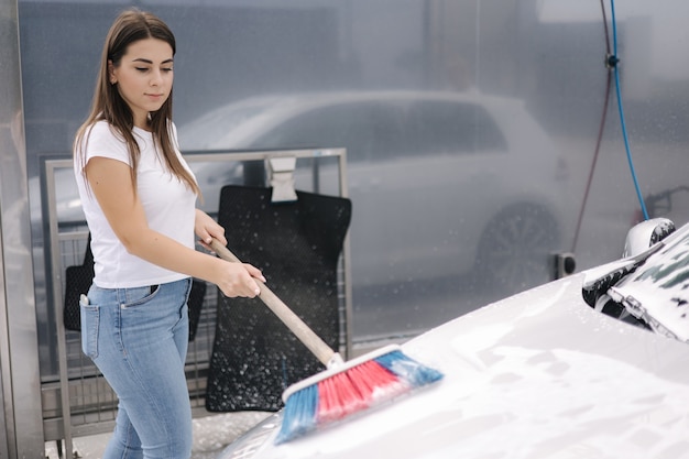 Aantrekkelijke jonge vrouw wast haar auto met shampoo en borstelt vrouw wast auto met schuim