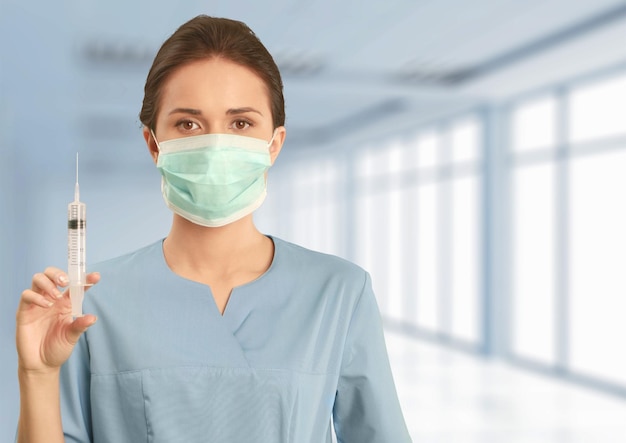 Aantrekkelijke jonge vrouwelijke arts met spuit op wazig ziekenhuis interieur op achtergrond
