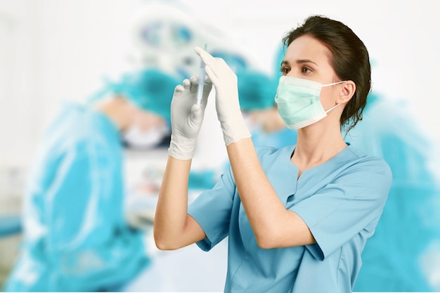 Aantrekkelijke jonge vrouwelijke arts met spuit op wazig ziekenhuis interieur op achtergrond