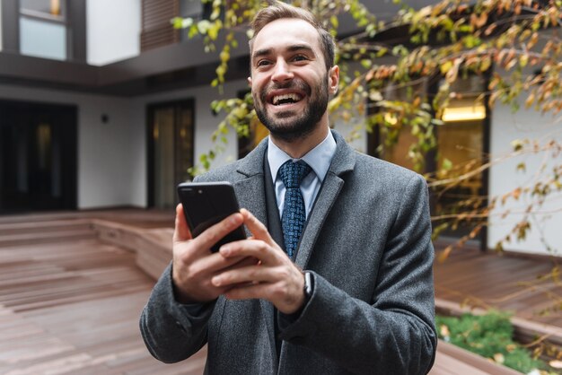 Aantrekkelijke jonge zakenman dragen pak buiten lopen, met behulp van mobiele telefoon