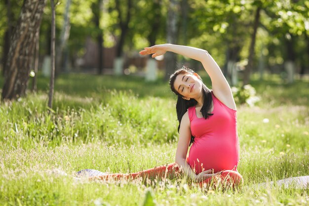 Aantrekkelijke jonge zwangere vrouw die yogaoefeningen in openlucht in het park doet. Verwacht dat een vrouw een gezonde en actieve levensstijl heeft.