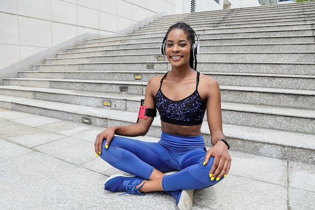 Aantrekkelijke jonge zwarte sportvrouw in buiten zitten in lotushouding en glimlachend in de camera