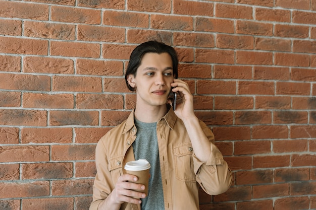 Aantrekkelijke jongeman praten op mobiele telefoon, met kopje koffie