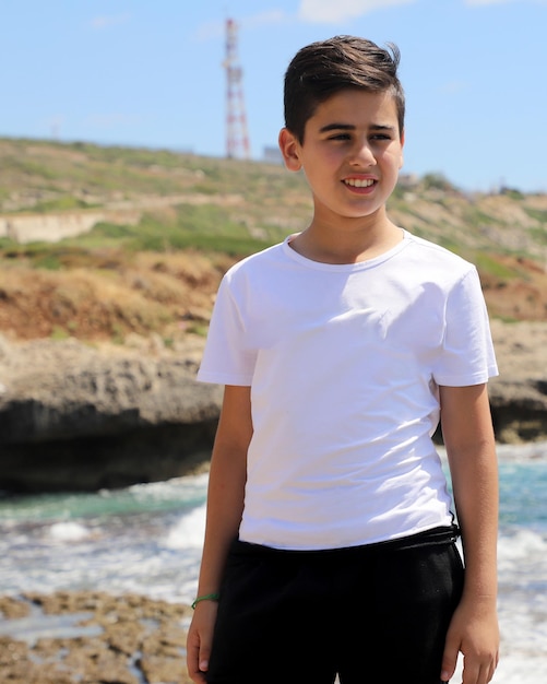 Foto aantrekkelijke jongen met een wit t-shirt op het rotsachtige strand foto mockup voor ontwerp