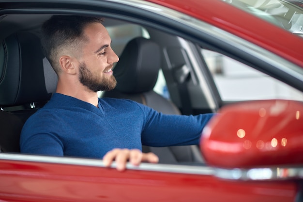 Aantrekkelijke klant die in blauwe sweater auto in salon kiezen.