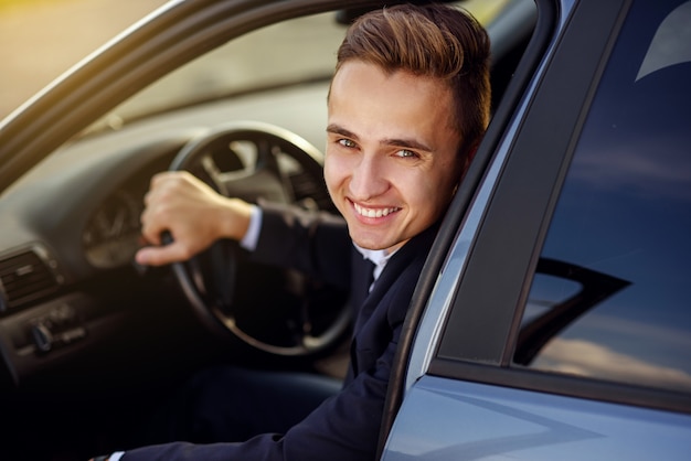 Aantrekkelijke knappe lachende man in een pak een dure auto rijden