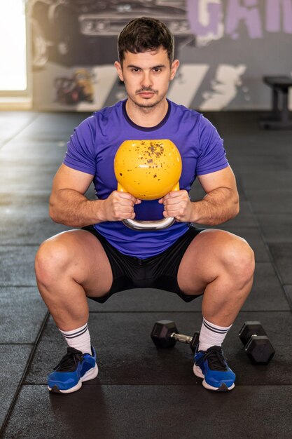 Aantrekkelijke knappe man die Kettlebell vasthoudt en squats doet in de moderne sportschool