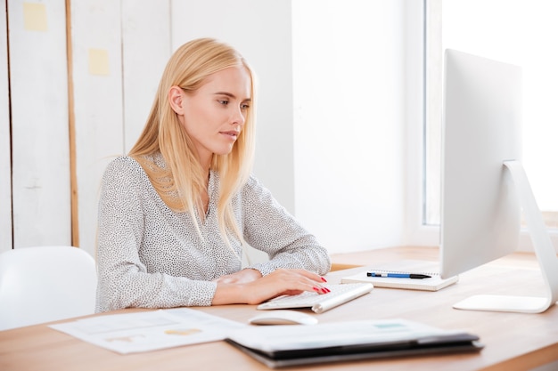 Aantrekkelijke lachende blonde zakenvrouw werken met laptop in office