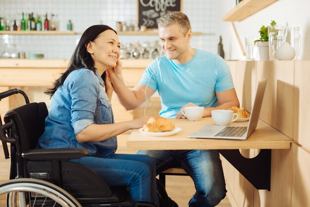 Aantrekkelijke lachende donkerharige gehandicapte vrouw en een knappe gelukkig blonde man zitten aan de tafel in een café en luisteren naar muziek en koffie drinken