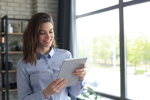 Aantrekkelijke lachende vrouw die werkt op een tablet in een kantoor aan huis.