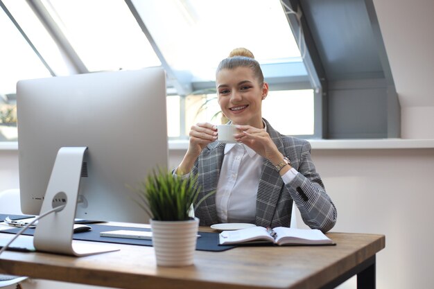 Aantrekkelijke lachende zakenvrouw zittend op kantoor met een kopje koffie.