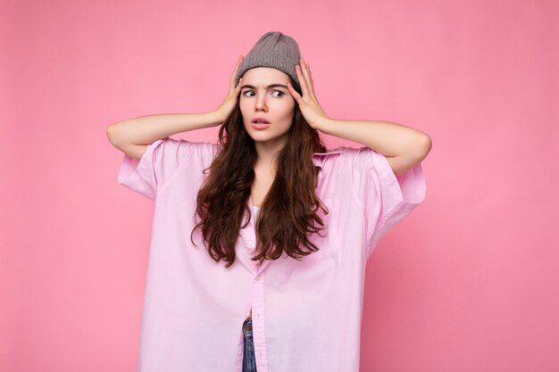 Aantrekkelijke leuke leuke schattige tedere jonge krullende donkerbruine vrouw die roze overhemd en grijze hoed draagt