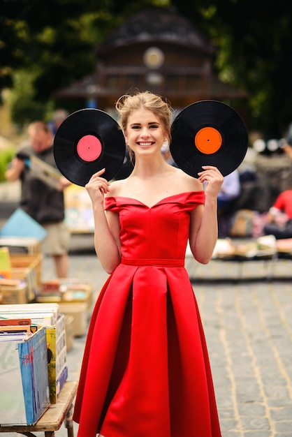 Aantrekkelijke leuke vrouw met een mooie glimlach in een rode jurk met een muziek vinylplaten