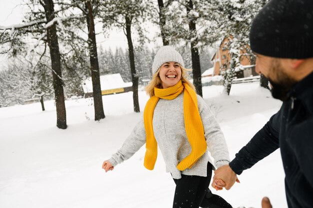 Aantrekkelijke man en vrouw knuffelen in het ijzige bos. Volwassen stel in truien heeft plezier tijdens het wandelen. Romantische date in de winter. Winter liefdesverhaal