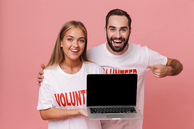 aantrekkelijke man en vrouw vrijwilligers die uniforme t-shirts dragen met een geïsoleerd laptopscherm