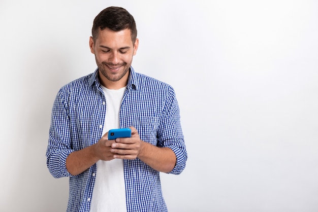 Aantrekkelijke mens die houdend een smartphone in zijn handen bevindt zich en het scherm bekijkt.