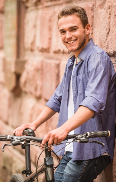 Aantrekkelijke mens die zich met zijn fiets dichtbij muur bevindt.