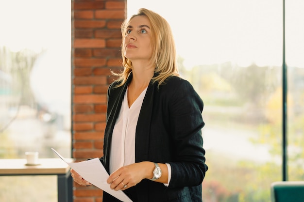 Aantrekkelijke mentor, zelfverzekerde jonge vrouw die in formele kledij papieren peinzend omhoog houdt.