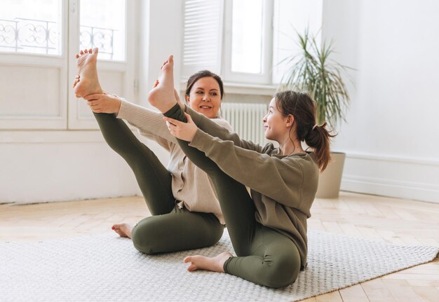 Aantrekkelijke moeder middelbare leeftijd vrouw en dochter tiener ptactice yoga samen in de lichte kamer