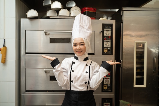 Aantrekkelijke moslimvrouw baker lachend naar de camera in de keuken van de bakkerij met grote oven