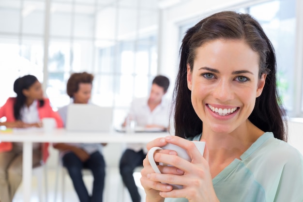 Aantrekkelijke onderneemster het drinken koffie met medewerkers op achtergrond