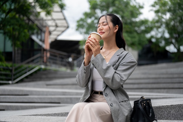Aantrekkelijke ontspannen Aziatische zakenvrouw geniet van haar koffie terwijl ze buiten op de trap zit