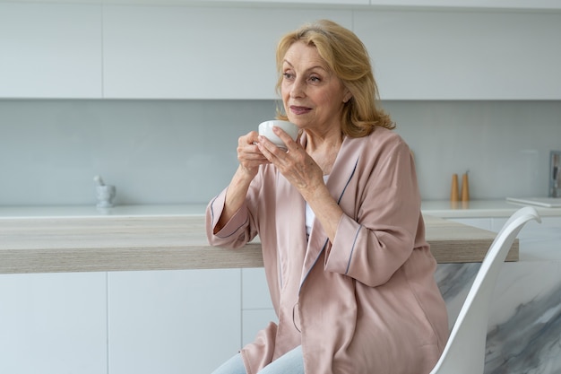 Aantrekkelijke oudere vrouw genietend van een kopje koffie in haar keuken denkend in waardering