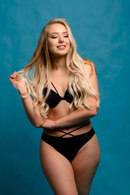 Aantrekkelijke plus size blonde vrouw In lingerie staande half gedraaid en glimlachend naar de camera, kopieer ruimte