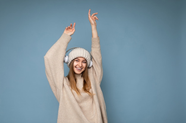 Aantrekkelijke positieve glimlachende jonge blonde vrouw, gekleed in beige winter trui en hoed geïsoleerd